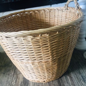 May include: A large, natural woven wicker basket with two handles. The basket is light brown and has a rounded bottom.