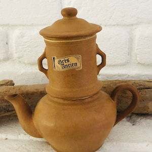 Könnte beinhalten: Eine braune Teekanne aus Keramik mit Deckel und zwei Henkeln. Die Teekanne trägt ein Etikett mit der Aufschrift "Gres Ancien".