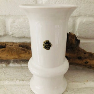 Könnte beinhalten: Weiße Keramikvase mit einem goldenen Etikett mit der Aufschrift "Delft's Wit".