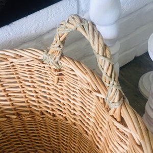 May include: A large, natural woven wicker basket with a single, thick woven handle. The basket is light brown and has a natural, rustic look.
