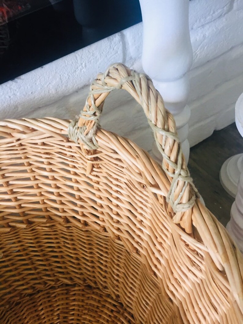 May include: A large, natural woven wicker basket with a single, thick woven handle. The basket is light brown and has a natural, rustic look.