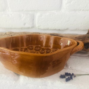 May include: A brown ceramic baking dish with a textured surface and a handle on each side. The dish is designed for baking cakes or other desserts.