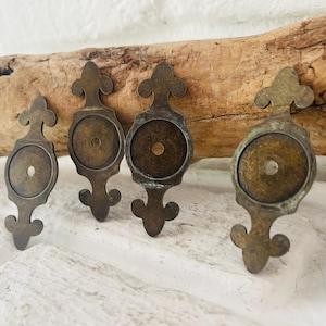 Könnte beinhalten: Vier antike Schubladengriffe aus Messing mit dekorativem Design. Jeder Griff hat eine kreisförmige Mitte mit einem kleinen Loch und eine dekorative Ober- und Unterseite. Die Griffe sind in einer Reihe angeordnet und zeigen ihre gealterte Patina.