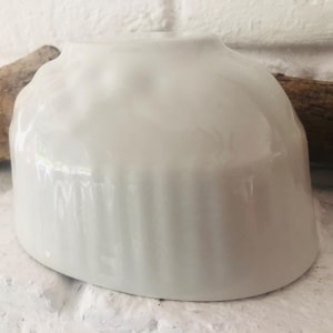 Könnte beinhalten: Weiße Keramikschüssel mit geriffeltem Design. Die Schüssel ist rund und hat eine glatte, glänzende Oberfläche.