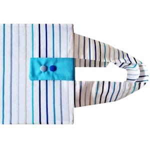 Könnte beinhalten: Eine weiße und blaue gestreifte Einkaufstasche mit einer türkisfarbenen Stoffklappe und zwei blauen Knöpfen. Die Tasche hat einen einzigen Henkel.