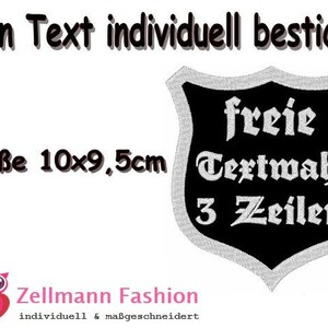 Pode incluir: Etiqueta bordada em preto e branco com a forma de um escudo. A etiqueta mede 10 cm por 9,5 cm e diz "freie Textwahl 3 Zeilen".