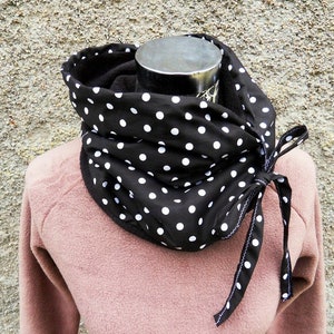 Könnte beinhalten: Ein schwarzer und weißer Polka-Dot-Infinity-Schal mit einer weißen Schleife. Der Schal ist aus einem weichen, bequemen Stoff gefertigt und perfekt, um sich im Winter warm zu halten.