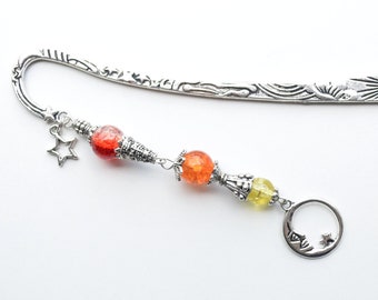 Könnte beinhalten: Silbernes Lesezeichen mit einem Sonnendesign oben und einem Monddesign unten. Das Lesezeichen hat drei Perlen, eine rote, eine orange und eine gelbe.