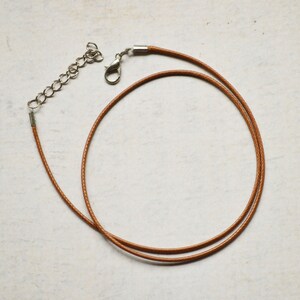 Könnte beinhalten: Eine braune Lederkordelkette mit einem silbernen Verschluss.