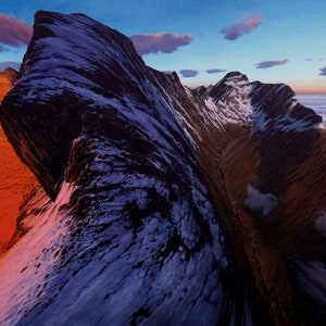 Puede incluir: Una vista panorámica de una cordillera cubierta de nieve al atardecer. Los picos son irregulares y dramáticos, con un valle profundo que los separa. El cielo es de un azul vibrante con vetas de nubes rosadas y naranjas. Las laderas inferiores de las montañas están cubiertas por una capa de nieve, mientras que el valle está lleno de una espesa capa de niebla.