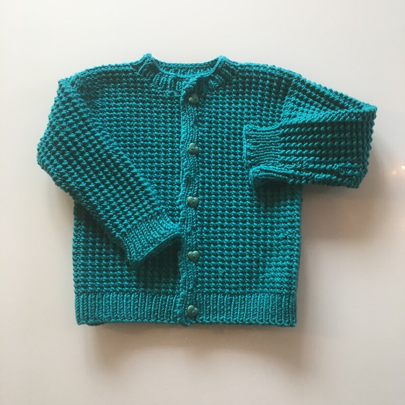 May include: A teal blue knitted cardigan with a button closure. The cardigan has a textured knit pattern.