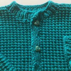 May include: A teal blue knitted cardigan with a button closure. The cardigan has a heart-shaped button.