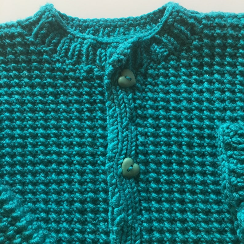 May include: A teal blue knitted cardigan with a button closure. The cardigan has a heart-shaped button.