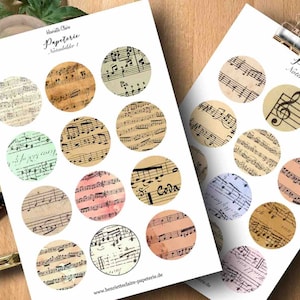 Könnte beinhalten: Zwei Papierbögen mit kreisförmigen Designs mit Vintage-Notenblättern. Die Kreise sind in verschiedenen Farben, darunter Beige, Rosa und Blau. Der Text "Henriette Claire Papeterie Notenbilder" ist auf den Blättern zu sehen. Ein Stift, eine Schere und ein kleines Etui befinden sich im Hintergrund.