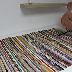 Könnte beinhalten: Bunt gewebter Teppich mit Streifenmuster. Der Teppich ist aus recyceltem Stoff gefertigt und hat einen Fransenrand.