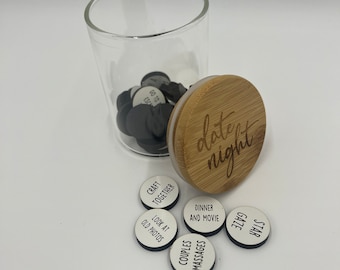 Könnte beinhalten: Ein Glasgefäß mit einem Bambusdeckel, auf dem "date night" steht. Das Gefäß enthält kleine weiße Kreise mit schwarzer Beschriftung. Die Kreise sagen "craft together", "look at old photos", "dinner and movie", "couples massages", "gaze", und "star".