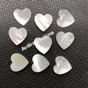 Op de afbeelding: Tien witte parelmoer hartvormige cabochons. De cabochons zijn glad en hebben een parelmoerglans.