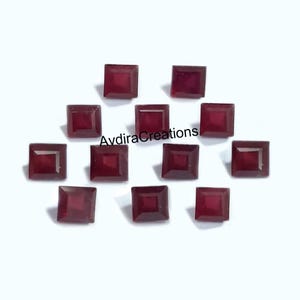 Może przedstawiać: Kolekcja kwadratowych, ciemnoczerwonych kamieni szlachetnych. Kamienie są ułożone na białej powierzchni, z widocznym tekstem "AvdiraCreations". Kamienie szlachetne są prawdopodobnie przeznaczone do tworzenia biżuterii lub rękodzieła.