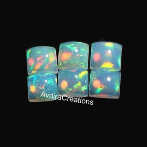 May include: Six square-shaped opal cabochons with iridescent colors, including green, blue, and orange. The cabochons are set against a black background.