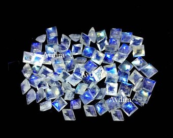 May include: A collection of iridescent white moonstone gemstones, cut into square shapes. The stones have a blue sheen and are arranged in a pile.