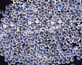 May include: A close-up view of a large quantity of small, round, clear gemstone beads with iridescent blue and green flashes. The beads are scattered on a black surface.