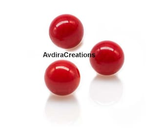 May include: Three glossy, round, bright red beads are scattered on a white surface. The beads have a smooth, reflective surface, with a small, bright highlight on each. The text "AvdiraCreations" is visible.