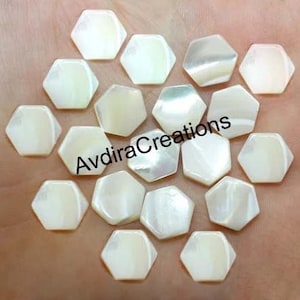 Puede incluir: Una colección de 20 cabujones hexagonales de nácar blanco. Los cabujones son lisos y tienen un ligero brillo iridiscente.
