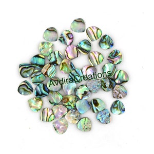 May include: A collection of iridescent abalone shell cabochons in various shapes and sizes. The shells display a range of colors, including blues, greens, and purples, with a pearlescent sheen. The text "AvdiraCreations" is visible.