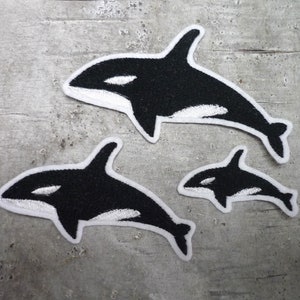 Könnte beinhalten: Drei schwarze und weiße Filz- oder Stoff-Orca-Wal-Aufnäher. Der größte Orca ist etwa 10 cm lang, der mittlere Orca ist etwa 7,5 cm lang und der kleinste Orca ist etwa 5 cm lang.