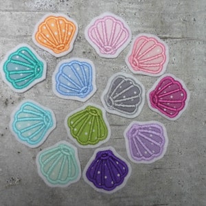 Könnte beinhalten: Sortiment von 11 bunten, gestickten Filzmuscheln mit weißen Punkten. Die Muscheln sind in verschiedenen Blautönen, Grün, Rosa, Lila und Orange.