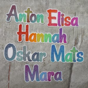 Könnte beinhalten: Sechs bunte gestickte Patches mit den Namen Anton, Elisa, Hannah, Oskar, Mats und Mara.