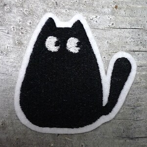 Könnte beinhalten: Schwarzer gestickter Bügel-Patch mit einem Katzenmotiv mit weißen Augen und einem weißen Umriss.