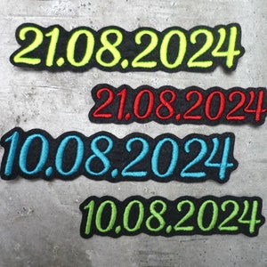 Könnte beinhalten: Vier gestickte Patches mit den Daten 21.08.2024 und 10.08.2024. Die Patches sind in verschiedenen Farben: Gelb, Rot, Blau und Grün.