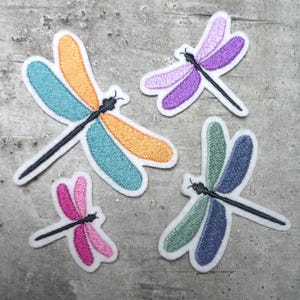 Könnte beinhalten: Vier gestickte Bügelbilder mit bunten Libellen-Designs. Die Libellen sind in den Farben Türkis, Orange, Lila, Rosa und Grün gehalten.