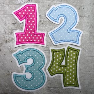 Könnte beinhalten: Vier Filzstoffzahlen, 1, 2, 3 und 4, mit einem weißen Sternmuster. Die Zahlen sind pink, blau, türkis und grün.