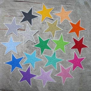 Könnte beinhalten: Eine Sammlung von 18 sternförmigen Stoff-Patches in verschiedenen Farben, darunter Rot, Blau, Grün, Gelb, Orange, Pink, Lila und Silber. Die Sterne sind in einem Kreis auf einer grauen Holzoberfläche angeordnet.