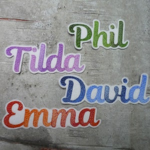 Könnte beinhalten: Fünf gestickte Stoffpatches mit Namen in verschiedenen Farben. Die Namen sind Phil, Tilda, David und Emma.
