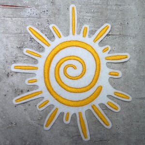 Könnte beinhalten: Eine gelbe gestickte Sonne mit einem Spiralmuster auf weißem Hintergrund.