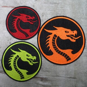Könnte beinhalten: Drei gestickte Bügelbilder mit einem Drachenmotiv. Die Patches sind rund und haben einen schwarzen Hintergrund. Die Drachen sind rot, orange und grün.