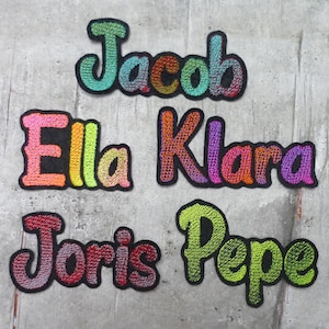 Könnte beinhalten: Fünf bunte gestickte Aufnäher mit den Namen: Jacob, Ella, Klara, Joris und Pepe. Die Aufnäher sind aus einem weichen, strukturierten Stoff gefertigt und haben ein leicht erhabenes Design.
