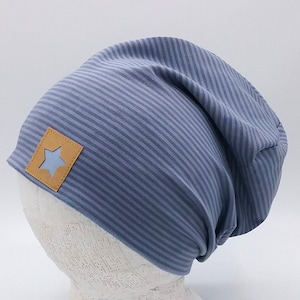 Könnte beinhalten: Eine blau gestreifte Beanie-Mütze mit einem hellblauen sternförmigen Aufnäher. Die Mütze ist aus weichem Stoff gefertigt und zum Tragen auf dem Kopf bestimmt. Die Mütze wird auf einem weißen Schaufensterkopf präsentiert.