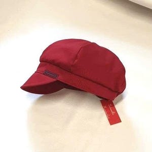 May include: A solid red newsboy cap with a black label that says "Isabelle Accessories".