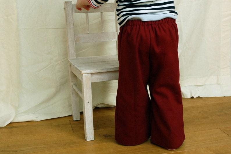 Pantalón infantil en alambique marítimo, pantalón marinero Fiete en rojo oscuro-burdeos, con pierna ancha, babero marinero derecho e izquierdo con botones. imagen 4