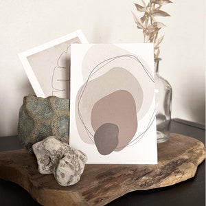 May include: A minimalist abstract art print with a white background and overlapping beige, brown, and gray shapes. The shapes are outlined in black lines.