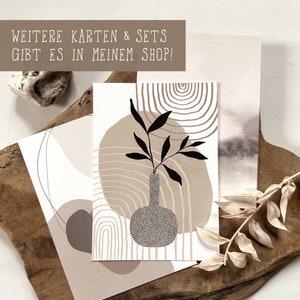 May include: A white card with a black and white illustration of a vase with a plant inside. The vase is surrounded by abstract shapes in beige and brown. The text "WEITERE KARTEN & SETS GIBT ES IN MEINEM SHOP!" is at the top of the card.
