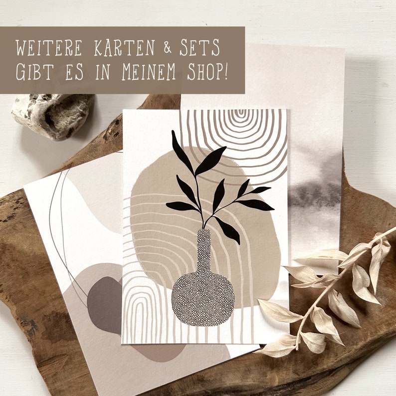May include: A white card with a black and white illustration of a vase with a plant inside. The vase is surrounded by abstract shapes in beige and brown. The text "WEITERE KARTEN & SETS GIBT ES IN MEINEM SHOP!" is at the top of the card.