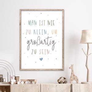 May include: A framed print with a white background and a light brown frame. The print features a quote in German that reads "Man ist nie zu klein, um großartig zu sein." which translates to "One is never too small to be great." The quote is written in a colourful, handwritten font with a small blue heart at the bottom.