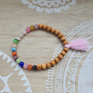 Könnte beinhalten: Ein farbenfrohes Perlenarmband mit einem rosa Quaste. Das Armband besteht aus Holzperlen und verfügt über eine Vielzahl von farbigen Steinen.