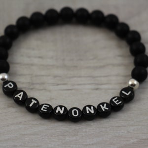 Könnte beinhalten: Schwarzes Perlenarmband mit silbernen Perlen und dem Wort "PATENONKEL" in weißen Buchstaben.
