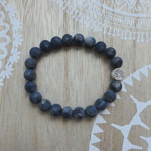 Könnte beinhalten: Ein schwarzes Perlenarmband mit einem silbernen Baum-Anhänger. Das Armband besteht aus runden, dunkelgrauen Perlen und hat einen silbernen Anhänger in Form eines Baumes.